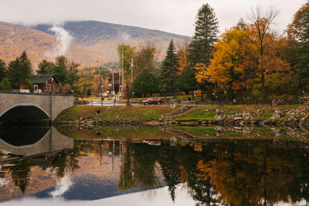 Idyllic autumn scene with a bridge over a reflective river, surrounded by colorful trees.